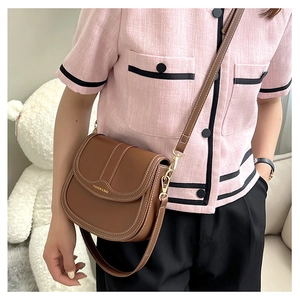 Detail of brown saddle bag with contrast stitching and gold 'FASHION & BAG' text