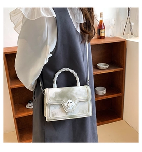 Detail of a chic crossbody bag with floral buckle and woven handle on a wood shelf