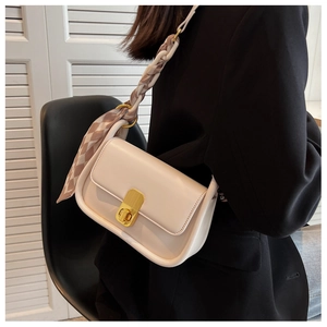 Détail d'un sac en cuir crème avec fermoir doré tournant et bandoulière foulard tressée