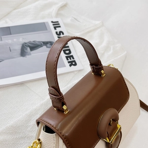 Detail of color-block handbag with brown leather handle and gold hardware on a magazine