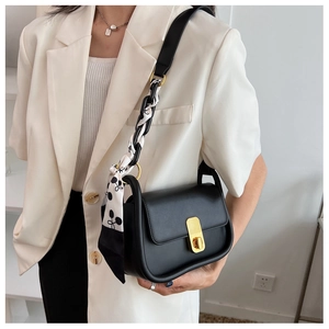 Détail du sac bandoulière en cuir noir avec fermoir doré et foulard en soie imprimé élégant