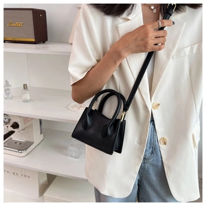 Détail d'un mini sac bandoulière noir en cuir avec boucle dorée sur un bureau