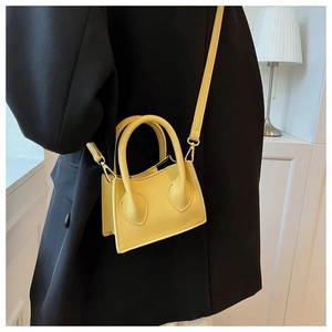 Détail d'un mini sac à main jaune vif avec accessoires dorés sur un blazer noir