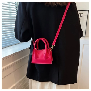 Vue macro d'un mini sac à main en cuir magenta porté sur un blazer noir avec détails dorés