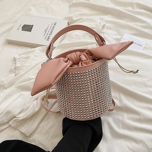Pink rhinestone bucket bag with oversized bow and metal studs on white fabric