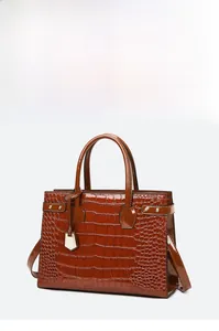 Close-up of glossy crocodile pattern texture and metal charm on dark brown handbag