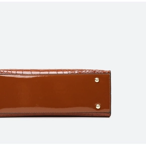 Detail of the brown patent leather handbag base with crocodile pattern and gold studs