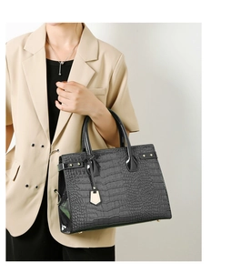 Close-up of black crocodile pattern leather handbag held by model in beige blazer