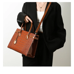Detail of brown crocodile pattern shoulder bag with polished handles and metal tag