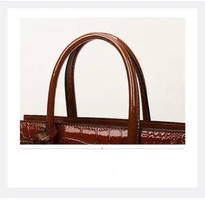 Detail of round handles on brown crocodile embossed patent leather tote handbag