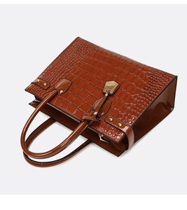 Macro view of brown crocodile-embossed tote bag with shiny finish and gold hardware