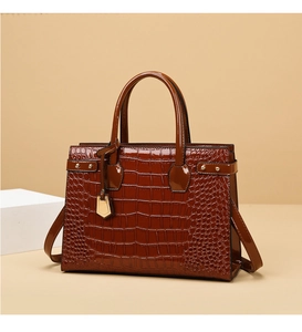 Detail of dark brown crocodile pattern handbag with glossy finish and gold metal hardware