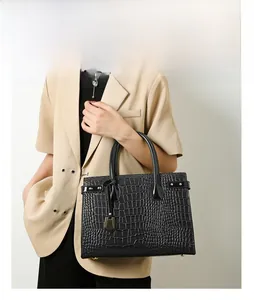 Detail of black crocodile pattern handbag with golden metal hardware and round dual handles
