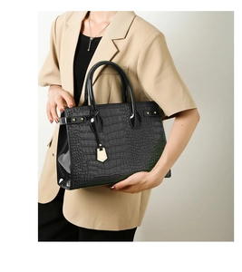 Detail of a structured black crocodile pattern handbag with gold hardware and top handles