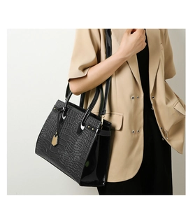 Model wearing a black crocodile-embossed tote bag with shiny patent leather side details