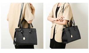 Detail of black crocodile-embossed tote bag with gold pendant and adjustable strap