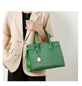Detail of emerald green crocodile embossed tote bag held by a model in a beige suit