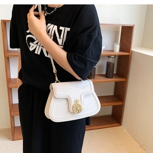 Detail shot of a white crossbody bag featuring a golden ship wheel buckle and stitching
