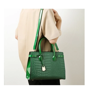 Detail of green crocodile pattern handbag showing long shoulder strap on model