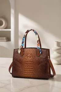 Detalle de bolso marrón con textura de cocodrilo y pañuelo decorativo en el asa
