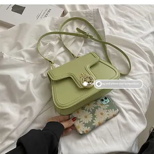 Size comparison of green square crossbody bag next to a smartphone on white fabric