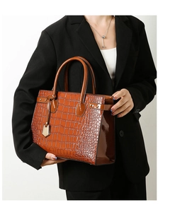 Detail of glossy brown crocodile embossed leather handbag with metal hardware accents