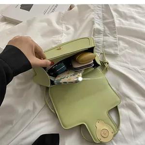 Top view of avocado green crossbody bag interior showing phone, makeup, and earphones