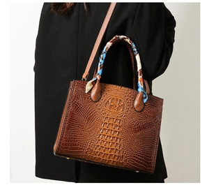 Detalle del bolso tote marrón con relieve de cocodrilo y pañuelo decorativo en asa