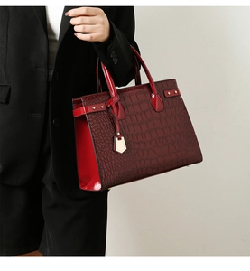 Detail view of burgundy tote bag with crocodile texture and golden shield pendant decoration