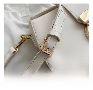 Detail of adjustable leather strap with gold hardware and fine stitching on white bag