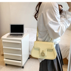 Detailed view of pale yellow leather shoulder bag with golden crown relief buckle