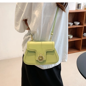 Light green crossbody bag with a gold crown buckle shown in a lifestyle indoor setting