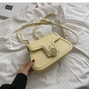 Close-up of cream square crossbody bag with vintage gold hardware on white fabric