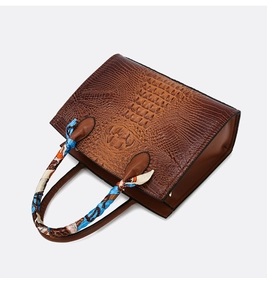 Detalle del bolso de mano marrón oscuro con grabado de cocodrilo y pañuelo de seda decorativo