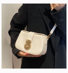 Detail of white leather shoulder bag with a gold circular clasp on a black suit blazer