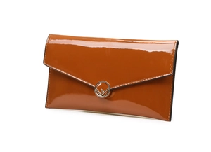 Detailed view of a brown patent leather clutch bag with a golden circular metal buckle