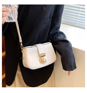Model wearing a minimalist cream crossbody bag with a gold buckle and black blazer