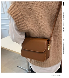 Detail of a brown leather crossbody bag with golden buckle shown on a model