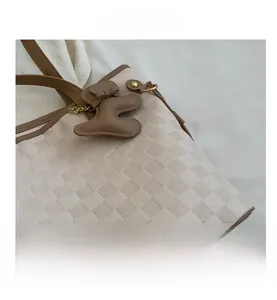 Close-up of beige checkered tote bag with brown leather trim and cute bear charm