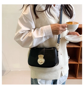 Model wearing a black leather shoulder bag with a gold round clasp in a lifestyle setting