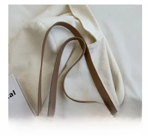 Detail of cream canvas tote bag showing brown leather handle and metal zipper closure