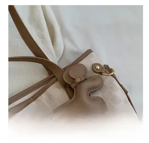 Detail of beige checkered tote bag with a brown bear charm and gold metal chain