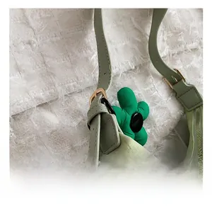 Detail of light green knitted shoulder bag featuring gold hardware and flower charm