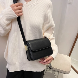 Close-up of black crossbody square bag with gold hardware worn over a striped sweater
