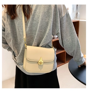 Detail view of a beige leather crossbody bag with an elegant golden teardrop twist lock