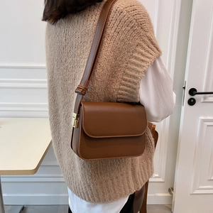 Caramel brown square crossbody bag with gold buckle and adjustable strap on a model