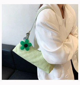 Close-up of light green pleated shoulder bag with a dark green floral plush charm