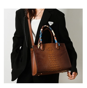 Bolso de mano marrón con grabado de cocodrilo y pañuelo decorativo usado por modelo
