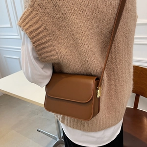 Brown leather crossbody square bag with gold buckle shown worn by a model in interior