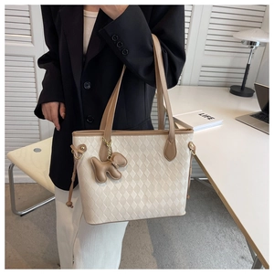 Detail of quilted beige tote bag with a leather dog charm in an office setting
